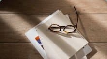 Reading glasses resting on a stack of papers on a sunlit desk