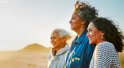 Three women standing together looking out over sunlit hills at golden hour